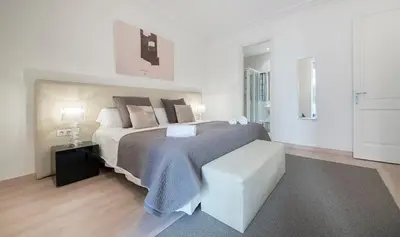 a white bedroom with a large bed and a stool at You Stylish Diagonal Apartments in Barcelona