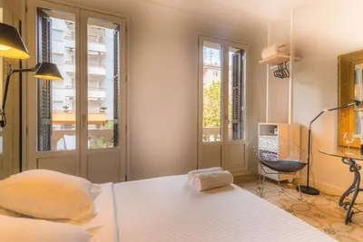 a bedroom with a bed and a desk and two windows at Habitació amb encant in Sitges