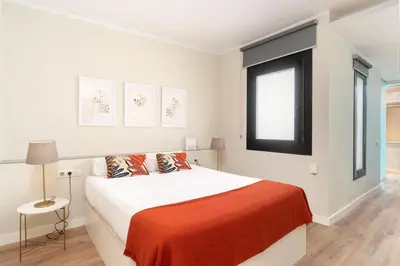 a white bedroom with a bed with an orange blanket at SibsBcn COLISEUM - Cozy and Central in Barcelona