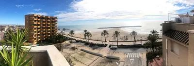 a view of a beach with palm trees and a building at Espectacular ático dúplex con vistas al mar in Cunit