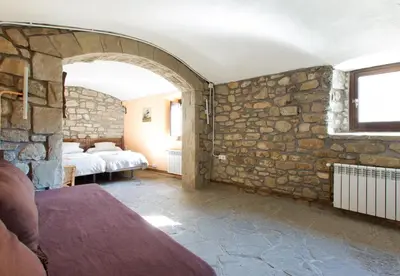 a bedroom with a stone wall with a bed and a window at Masia el Prat in El Pont de Vilomara