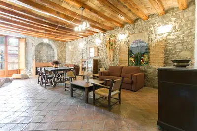 a living room with tables and chairs and a stone wall at Masia el Prat in El Pont de Vilomara