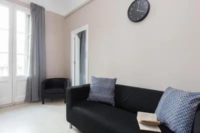 a living room with a black couch and a clock on the wall at Key Barcelona HOUSING (Carrer Girona) in Barcelona