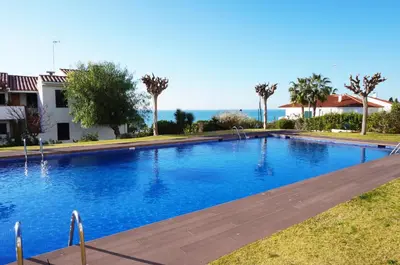 a large blue swimming pool with palm trees and the ocean at Cala Balmins Sea View in Sitges