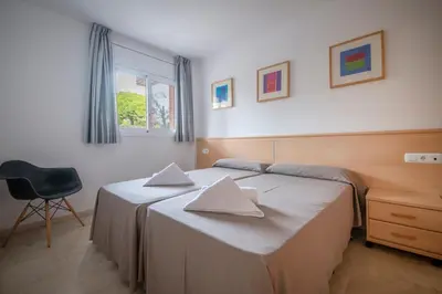 a bedroom with two beds and a chair and a window at Aparthotel Marsol in Castelldefels