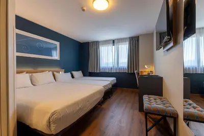 a hotel room with two beds and a chair at Travelodge Barcelona Poblenou in Barcelona