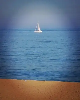a sail boat in the ocean with a beach at Rambla Poblenou&Mar Bella Beach in Barcelona