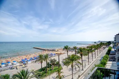 a beach with palm trees and umbrellas and the ocean at Blue sea front by Hello Homes Sitges in Sitges