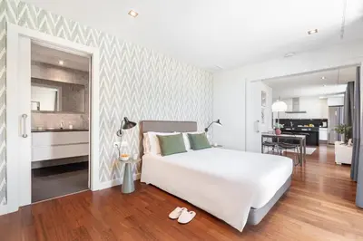 a bedroom with a large white bed and a kitchen at Aspasios Paseo de Gracia Apartments in Barcelona