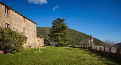 an old stone building with a fence and a tree at Masia de Vallforners in Tagamanent