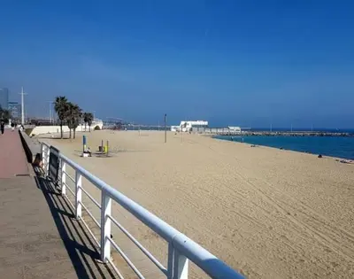 a sandy beach with a white fence and the ocean at Confort apartamentos en playa, 3 DRM in Barcelona
