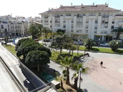a man walking in a park with palm trees in front of a building at Hotel Alexandra Sitges in Sitges