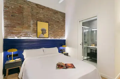a bedroom with a white bed and a brick wall at Arte Suites by Olala! - Smart Stay in Hospitalet de Llobregat