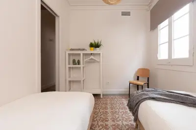 a white bedroom with two beds and a chair at Casa Cosi - Francoli 1 in Barcelona