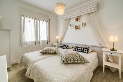a white bedroom with two beds and two windows at Vivalidays ilaria - Calella in Calella
