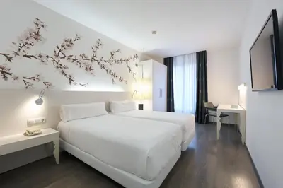 a white bedroom with a large white bed and flowers on the wall at Catalonia La Boquería in Barcelona
