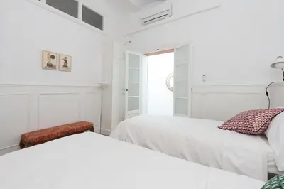 a white bedroom with two beds and a window at Casa Cosi - Eixample 1 in Barcelona