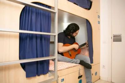 a man sitting on a bunk bed playing a guitar at Rocket Hostels Gracia in Barcelona