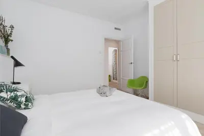 a white bedroom with a white bed and a green chair at Casa Cosi - Eixample 3 in Barcelona