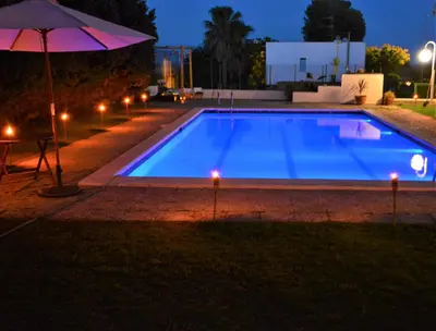 a large blue swimming pool at night with an umbrella at Villa Sitges Colibri at 10 min Walk Beaches - Center City Amaizing Garden Pool XXL Private Tenis Piste in Vilanova i la Geltrú