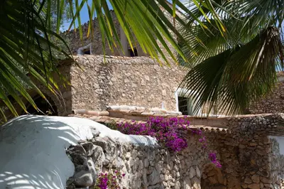 a stone wall with purple flowers next to a building at Casa Olivo at Masia Nur Sitges, Adults only in Canyelles