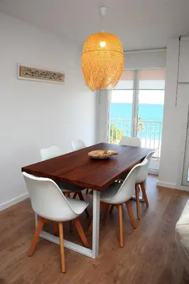 a dining room table with white chairs and a chandelier at Apartamento frente al mar in Canet de Mar
