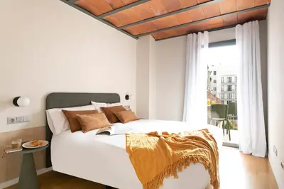 a white bedroom with a large bed with brown pillows at Aspasios Las Ramblas Apartments in Barcelona