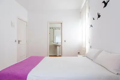 a white bedroom with a large white bed with purple sheets at Monrooms Barcelona in Barcelona