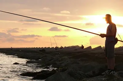 a man standing on the rocks holding a fishing rod at Casa Bella Vista en montaña con vistas al mar y piscina privada in Cunit