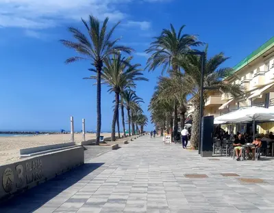 a sidewalk with palm trees and people sitting at tables at APARTAMENTO EN SEGUNDA LINEA DE MAR, WIFI & A.C in Cubelles