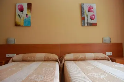 two beds in a bedroom with two paintings on the wall at Hostal Cal Siles in El Prat de Llobregat