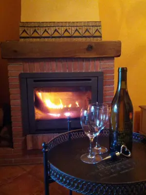 a bottle of wine and glasses on a table in front of a fireplace at Ca L'Estrada in Sant Esteve de Palautordera