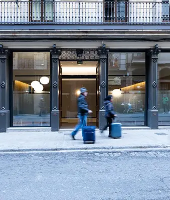 two people walking down the street with luggage in front of a store at Hotel Raval House in Barcelona