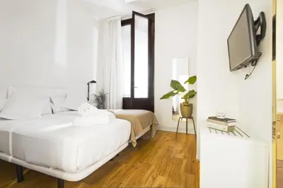 a white bedroom with a bed and a tv at Som Nit Born in Barcelona