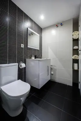 a bathroom with a white toilet and black tiles at Gran Apartmento Playa Badalona in Badalona