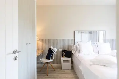 a white bedroom with a bed and a chair at Chic Gran Via Apartment in Barcelona