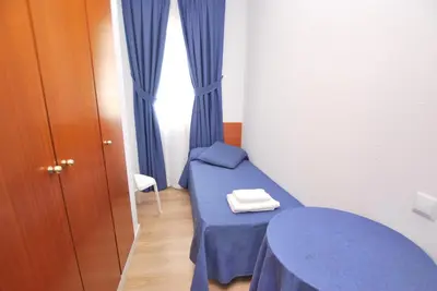 a small room with a blue bed and curtains at Hotel Tres Leones in Vilassar de Mar