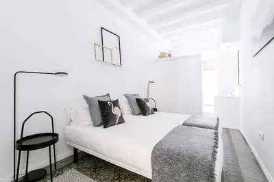 a white bedroom with a white bed and a black stool at Exquisite&historic Flat With Rooftop in Barcelona