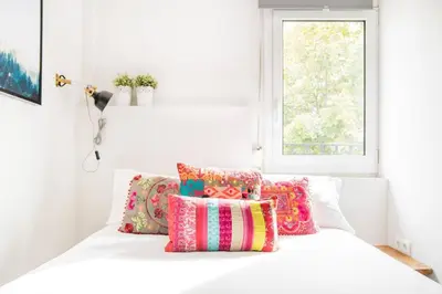 a white bed with colorful pillows and a window at Charming Apartment With Vibrant Accents in Hospitalet de Llobregat