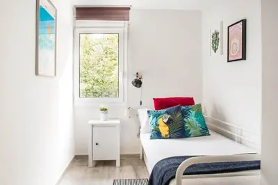 a small white room with a bed and a window at Charming Apartment With Vibrant Accents in Hospitalet de Llobregat