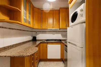 a small kitchen with wooden cabinets and a white refrigerator at Cozy & Central Apartment in Barcelona