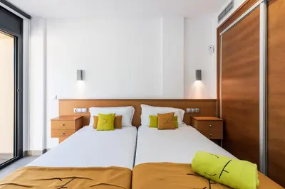 a bedroom with a large white bed with green pillows at Aparthotel Las Palmeras Castelldefels in Castelldefels
