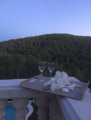 a table with two wine glasses and flowers on a balcony at Villa Paradise , playa privada a 10 minutos de Sitges in Sant Pere de Ribes