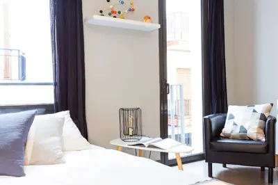 a bedroom with a bed and a chair next to a window at Bo&Co Apartments in Sitges