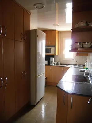 a kitchen with a white refrigerator and wooden cabinets at Atico Soleado Vistas panoramicas in Hospitalet de Llobregat