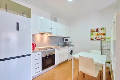 a kitchen with white cabinets and a table and a refrigerator at Precioso Loft en Badalona Centro in Badalona