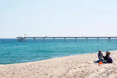 two people sitting on the beach with a pier in the background at Apartamento Cerca del Mar in Badalona
