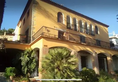 a large yellow building with balconies and palm trees at Medieval tower & villa by the sea in Caldes d'Estrac