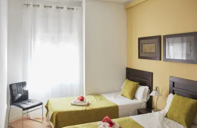 a bedroom with two beds and a chair and a window at Alcam Valencia II in Barcelona
