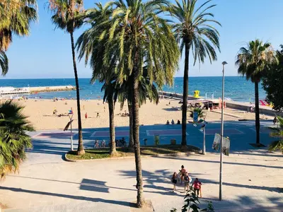 a group of people walking on a beach with palm trees at Fragata Beach Seaview in Sitges